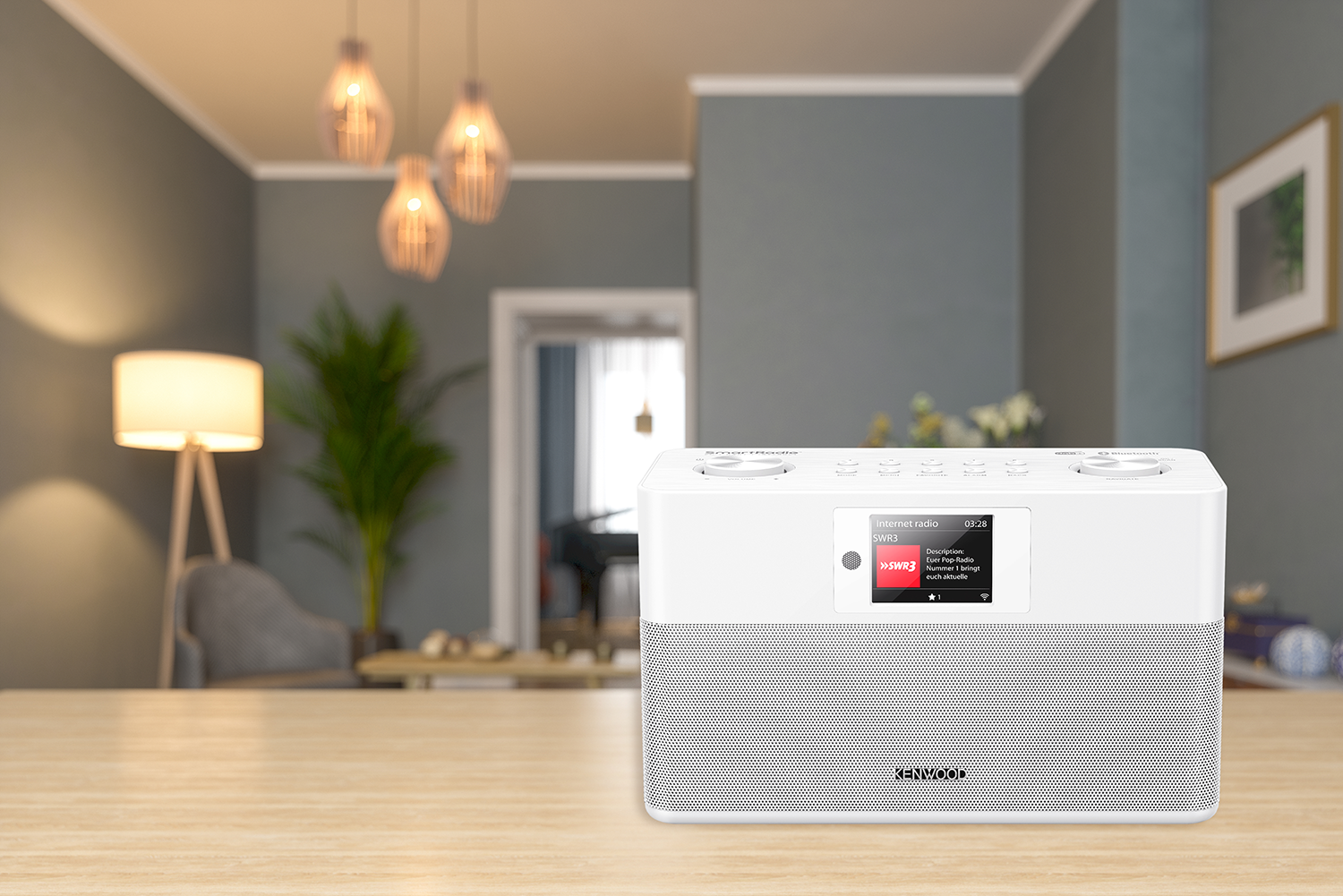 A white Kenwood radio is on a wooden table in a bright living room with a wooden table and pendant lights.