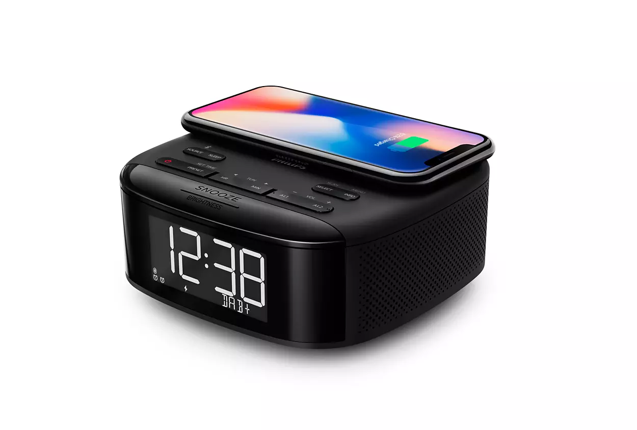 A black clock radio with a phone charging on top, showing the time and charging status.