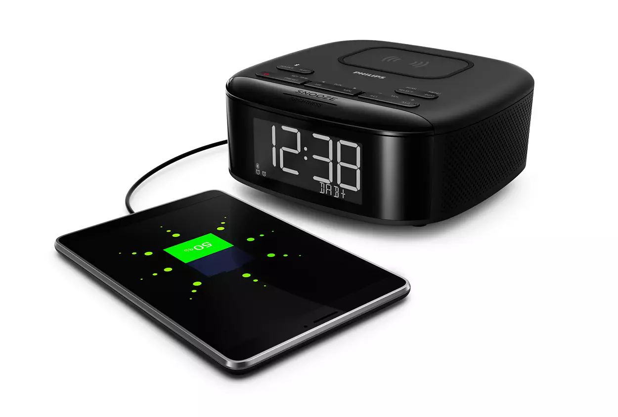 Black digital alarm clock and a tablet charging with a green 50% indicator on a white surface.
