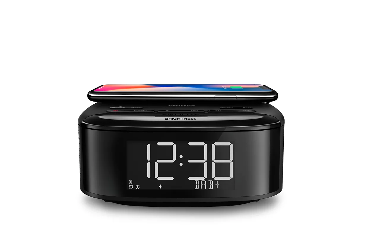 Black bedside clock with a phone on top, displaying the time and a wireless charging symbol.