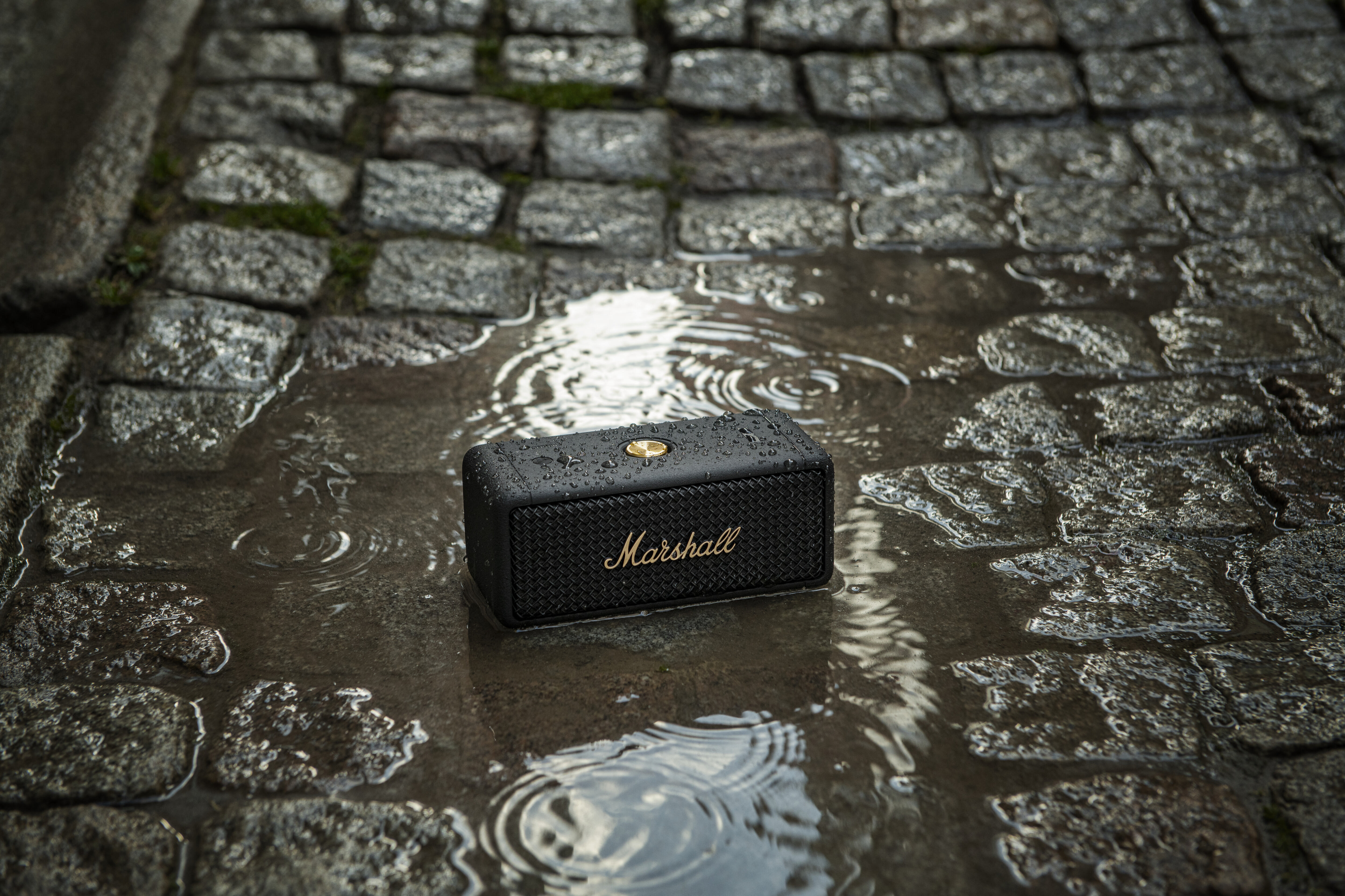 Ein kleiner schwarzer Marshall-Lautsprecher liegt im Regen auf einem nassen Kopfsteinpflaster.