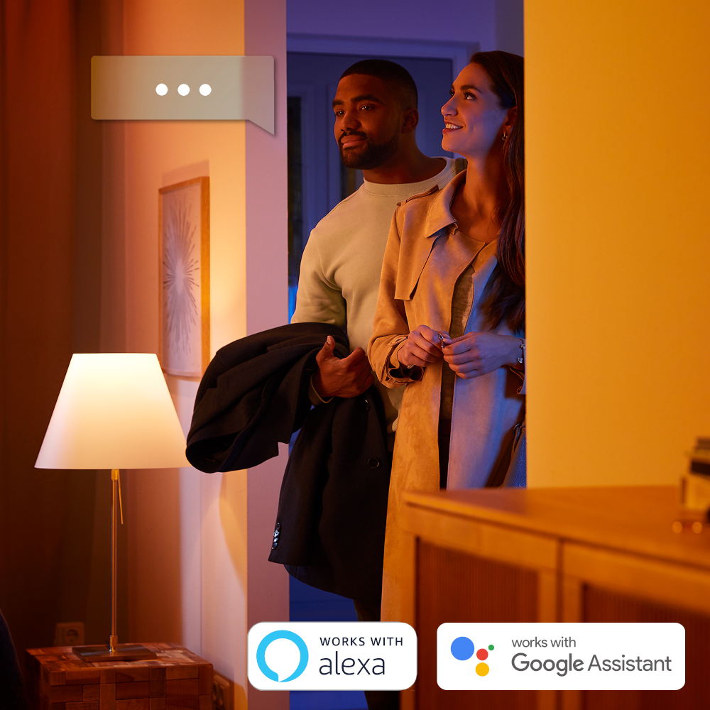 A couple stands in a doorway. A man holds a jacket. A lamp is on in the foreground. Speech bubble above.