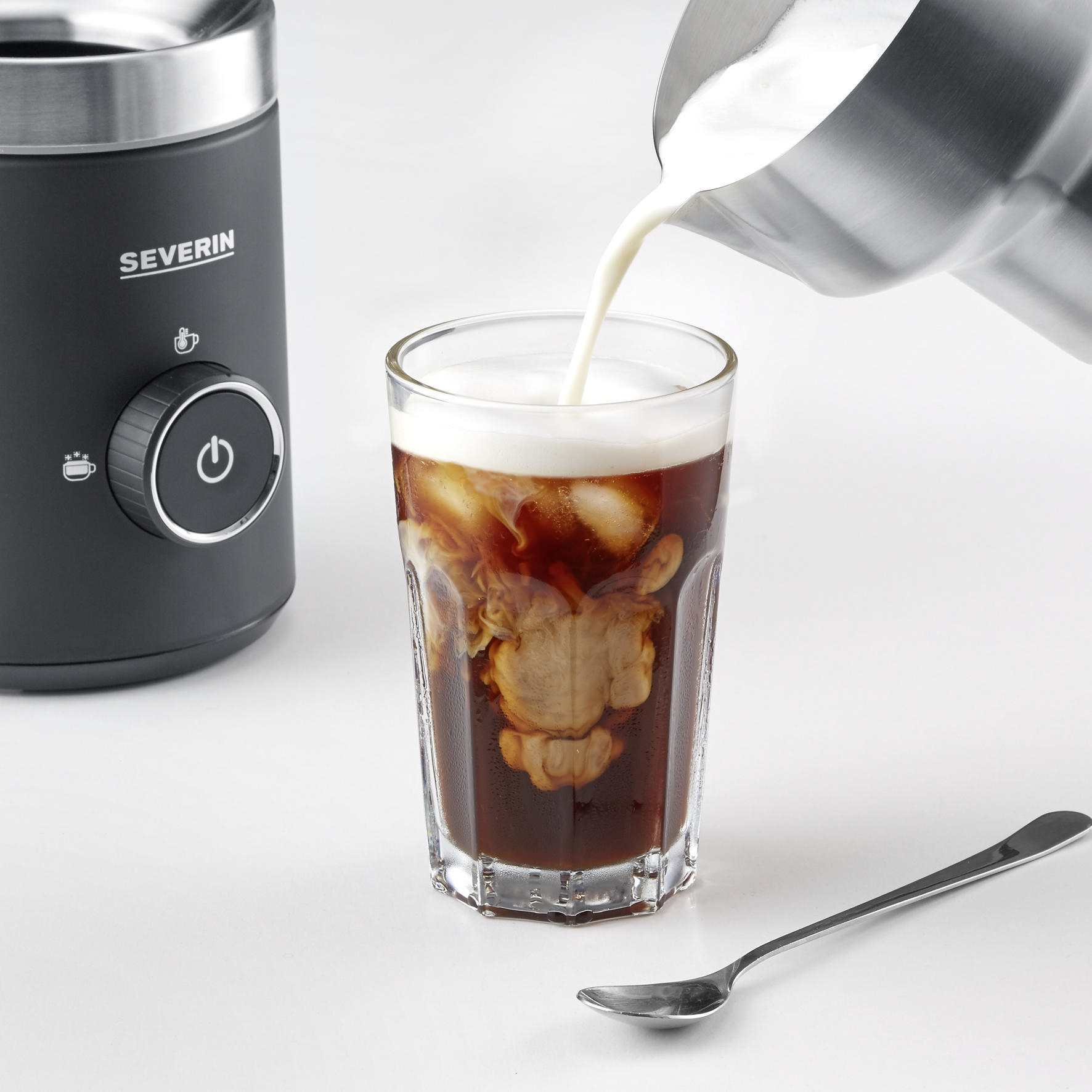 Milch wird in ein Glas mit Eiswürfeln und Kaffee gegossen.