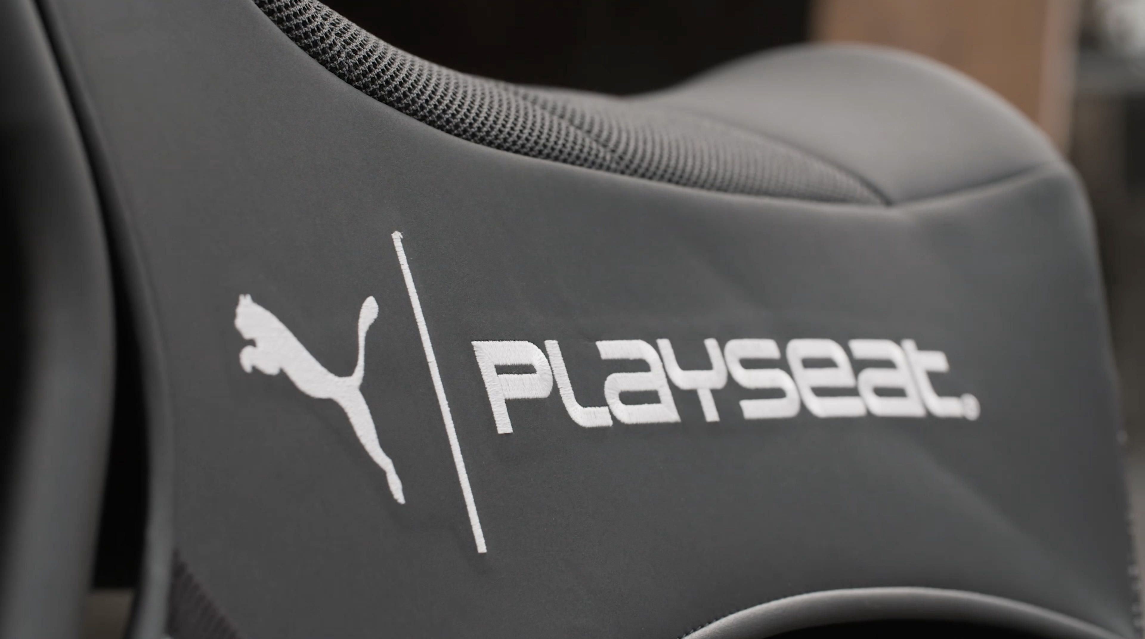 Grauer Playseat-Gaming-Stuhl mit Puma-Logo. Weißer Text auf dem Sitz. Schwarzer Hintergrund.