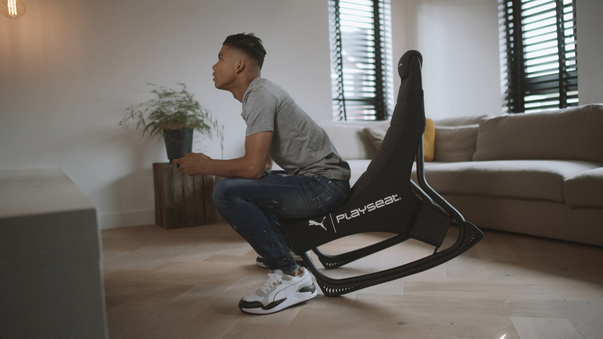 Mann in grauem Hemd und Jeans sitzt auf einem Puma Playset Gaming-Stuhl, hält einen Controller.