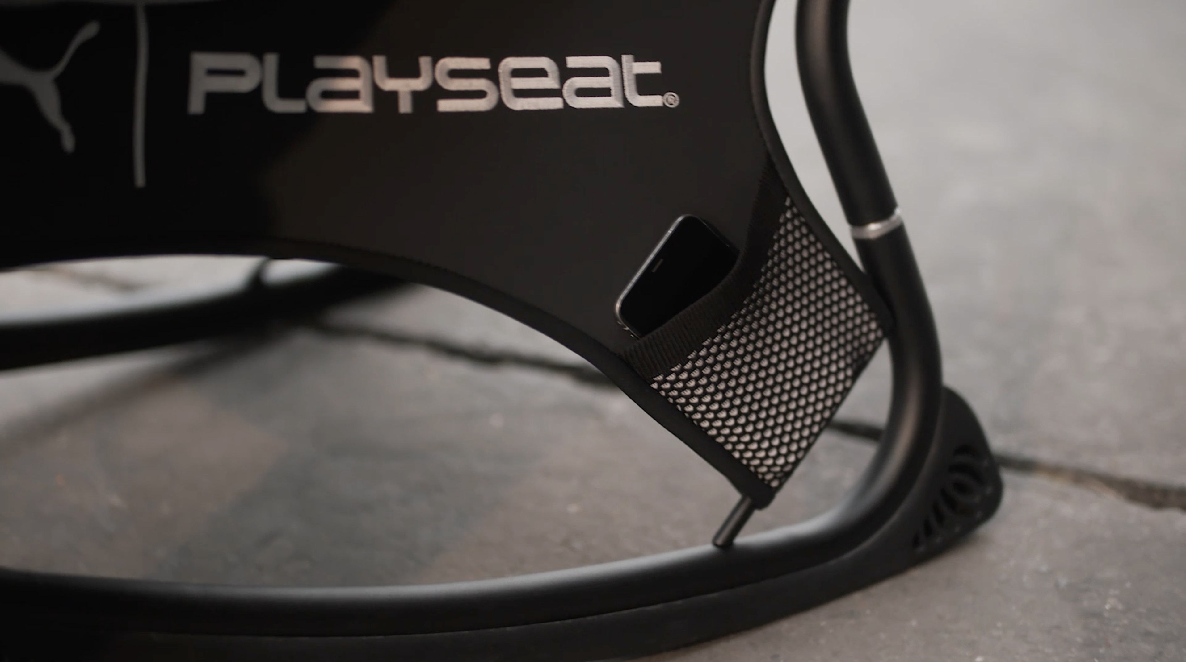 Schwarzer Playseat-Gaming-Stuhl mit einem Telefon in der Netztasche.