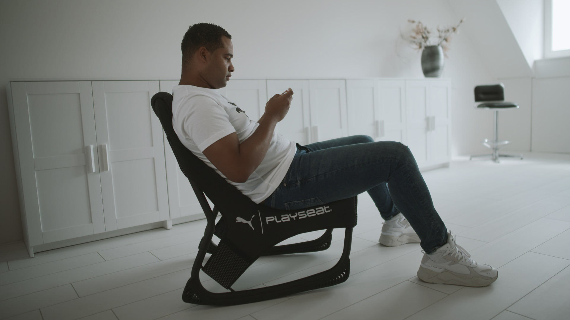 Mann sitzt in einem Gaming-Stuhl und spielt mit einem Controller. Ein Fernseher steht davor.
