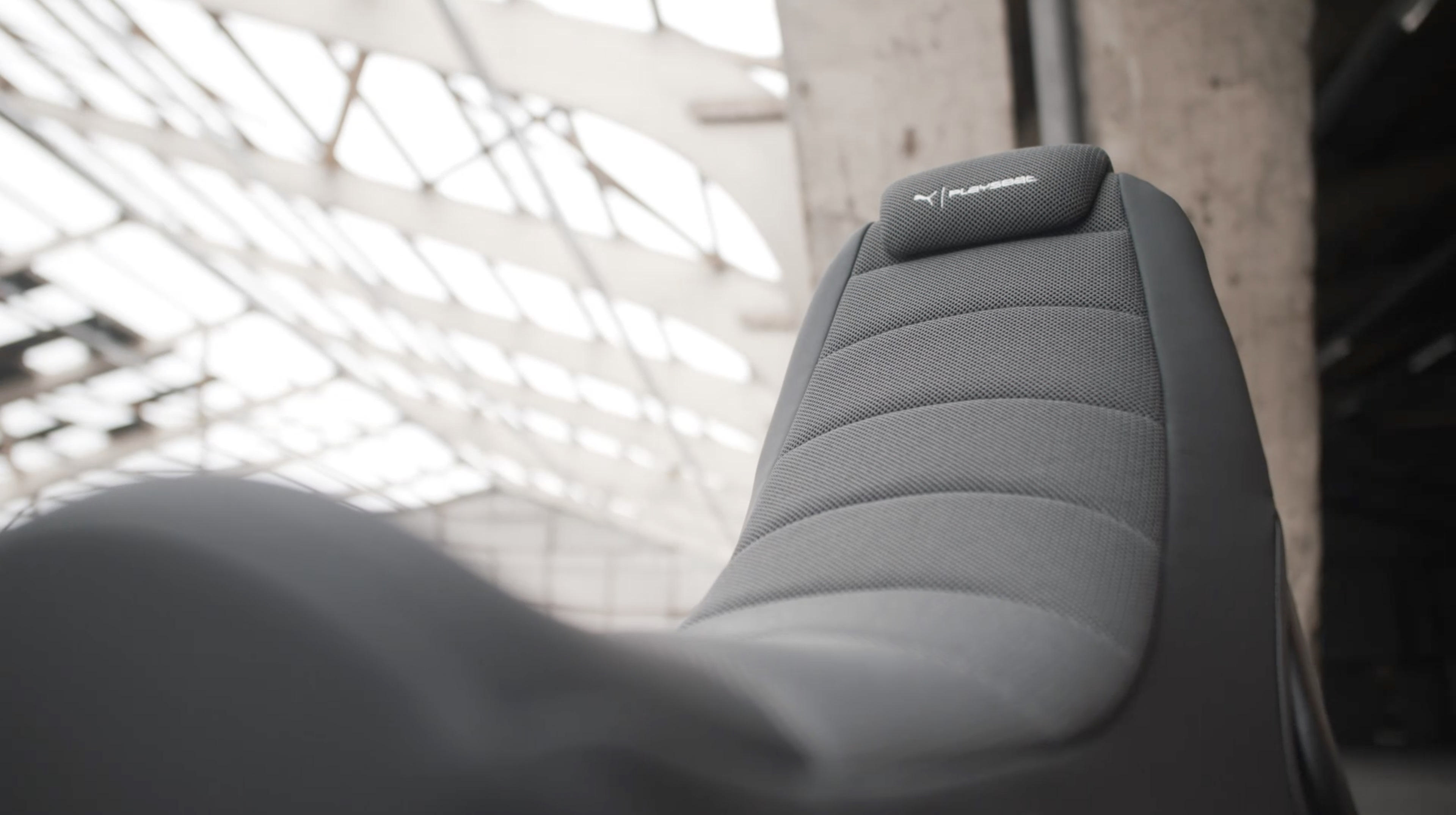 Grauer Stuhl mit Logo, in einem Gebäude. Die Umgebung ist industriell.