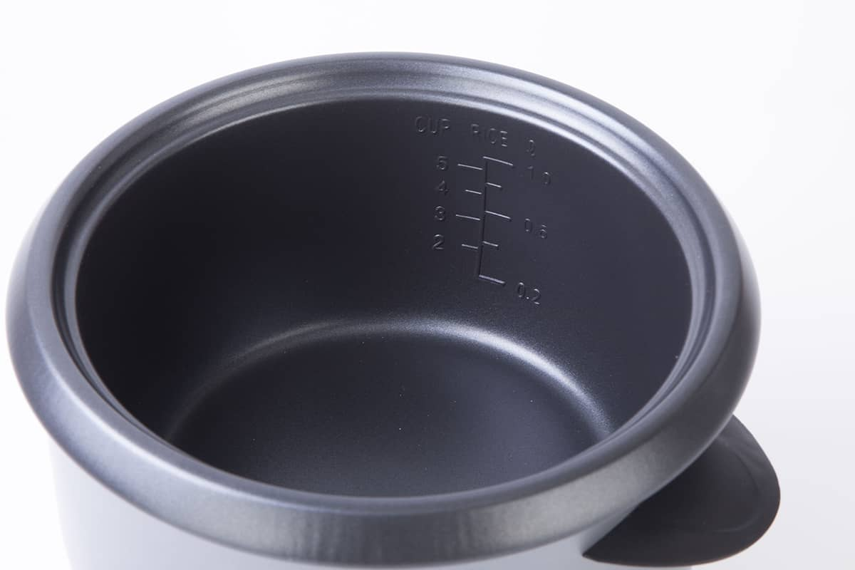 Una olla de arrocera negra, vista interior con marcas de medición, sobre blanco, vista superior.