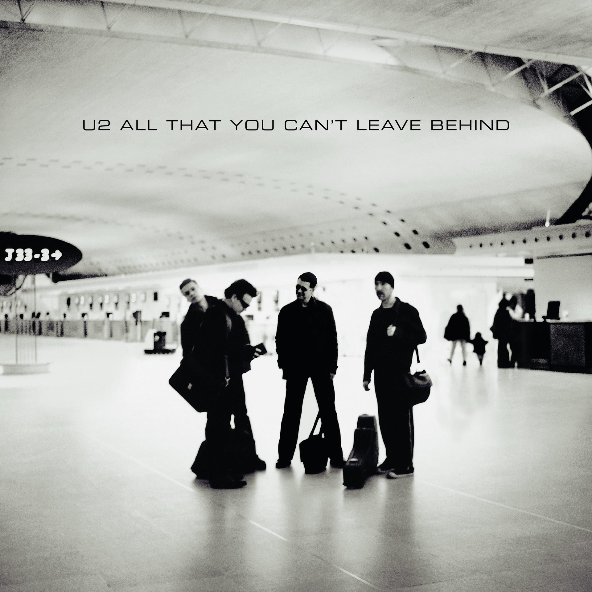U2 albumhoes. Bandleden lopen in een moderne luchthaven.