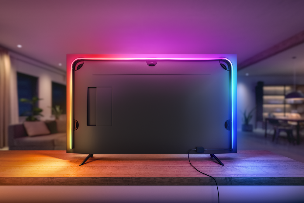 Parte trasera de TV con tiras LED de colores en bordes, sobre mesa de madera en habitación.