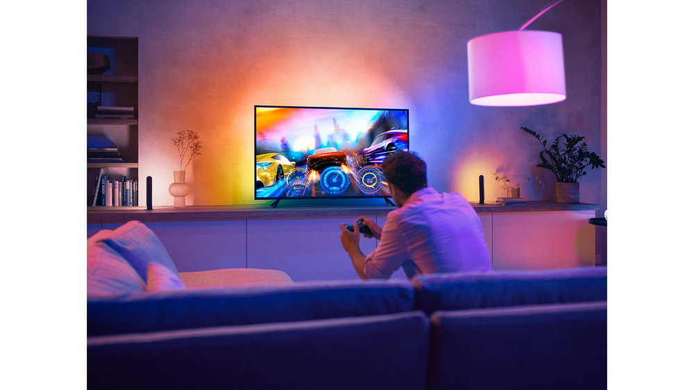 Un hombre juega un videojuego en un televisor. Es un juego de carreras con luces de colores.