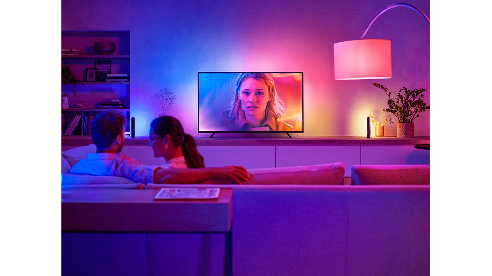 Una pareja viendo la televisión en una sala de estar con luces de colores. La mujer mira la TV.