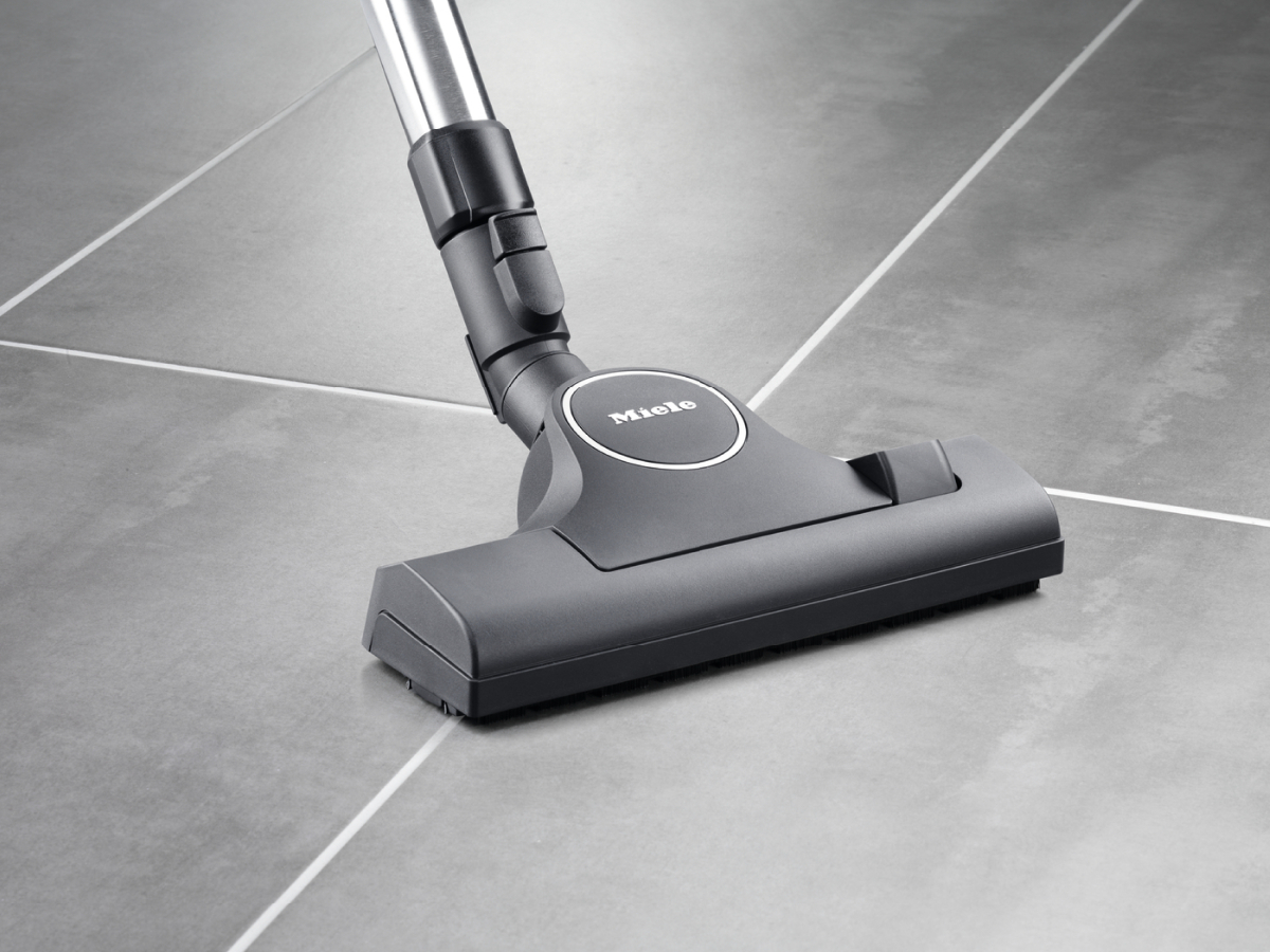 Ein Staubsaugerkopf auf einem grau gefliesten Boden, mit dem Miele-Logo sichtbar.
