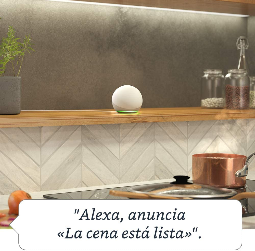 Un Echo Dot en una cocina, con una cita en español: 'Alexa, anuncia que la cena está lista'.