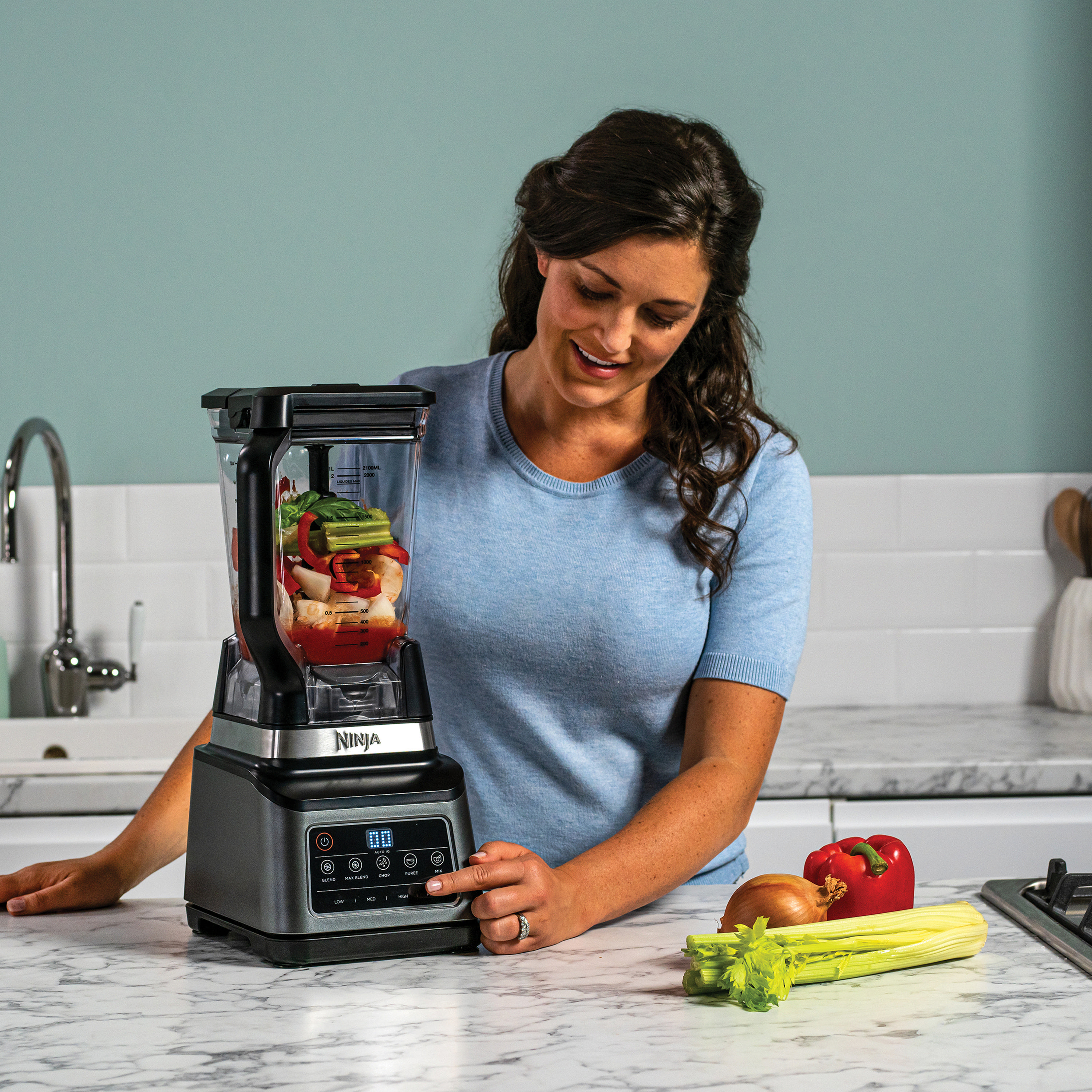 Frau benutzt einen Ninja-Mixer. Zutaten wie Gemüse und Früchte sind im Mixer.