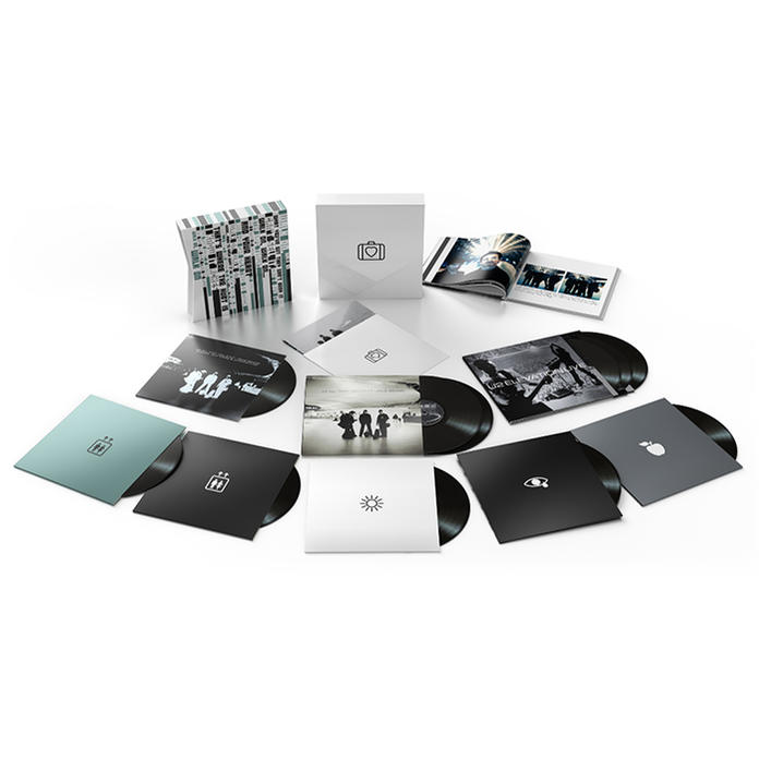 Boxset van vinylplaten met verschillende albumhoezen en een boekje, allemaal op een wit oppervlak.