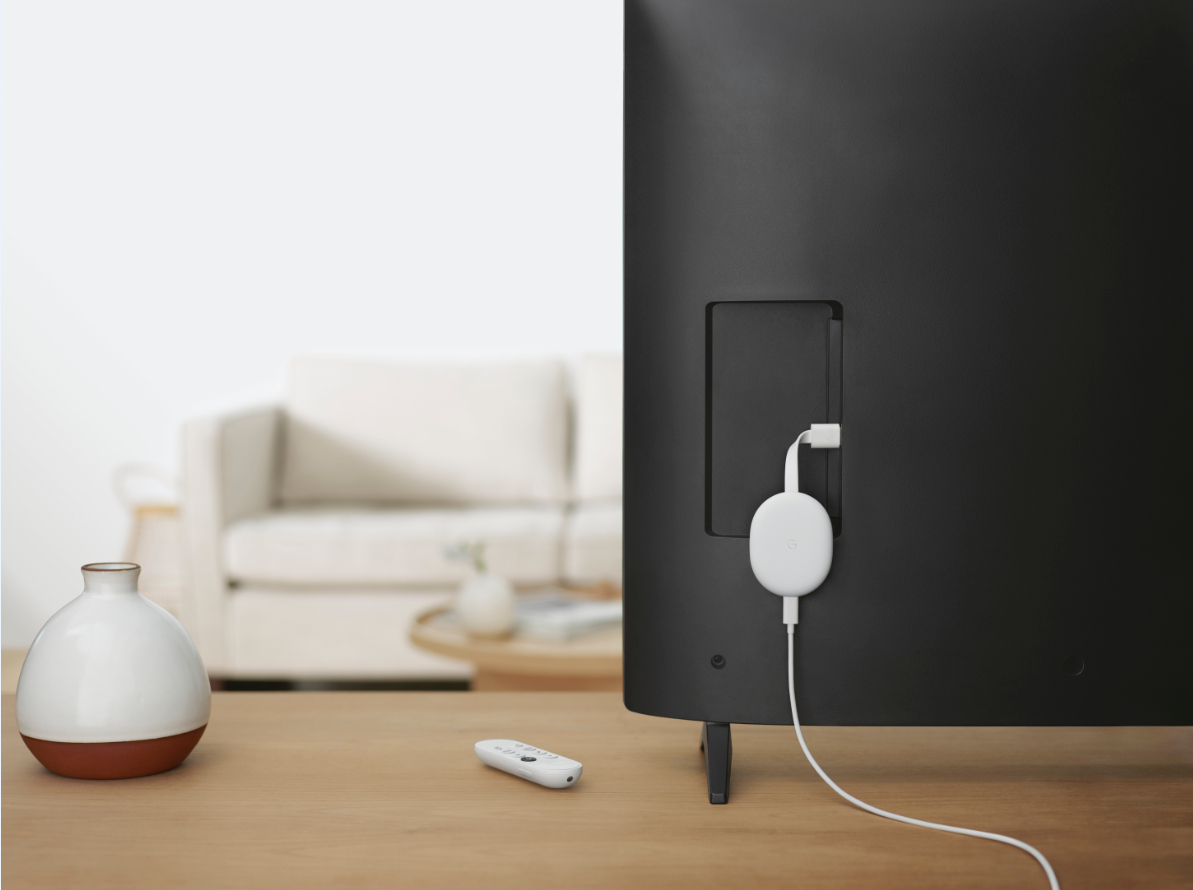 Ein Fernseher mit angeschlossenem Chromecast. Eine weiße Fernbedienung und eine Vase stehen auf einem Tisch.