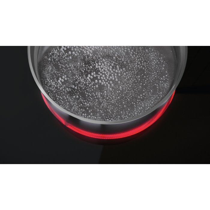 Una olla de vidrio con agua hirviendo sobre una estufa negra con un elemento calefactor rojo.