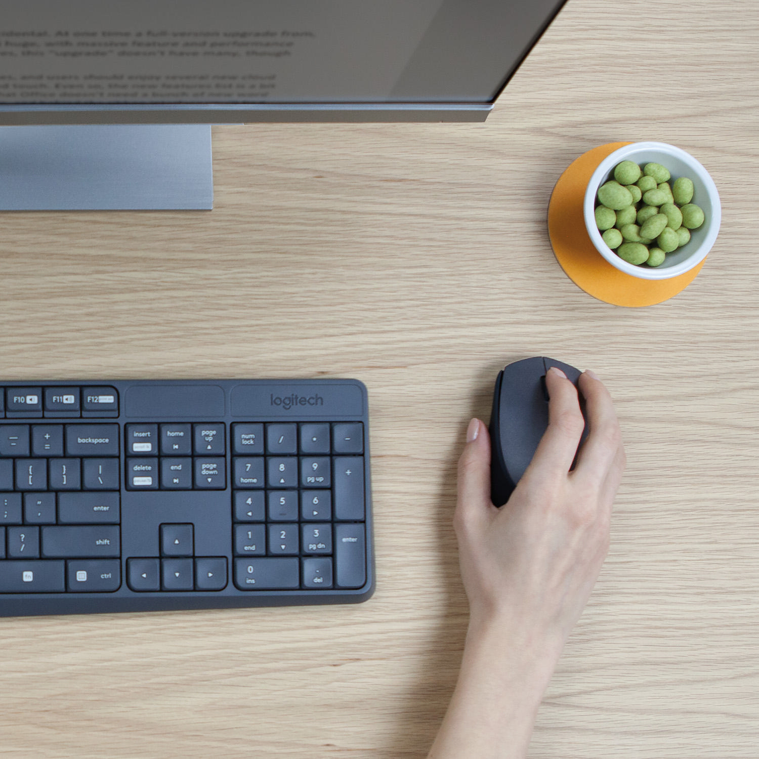 Ein Schreibtisch mit Tastatur, Maus und einer kleinen Schüssel mit grünen Snacks neben einem Computermonitor.