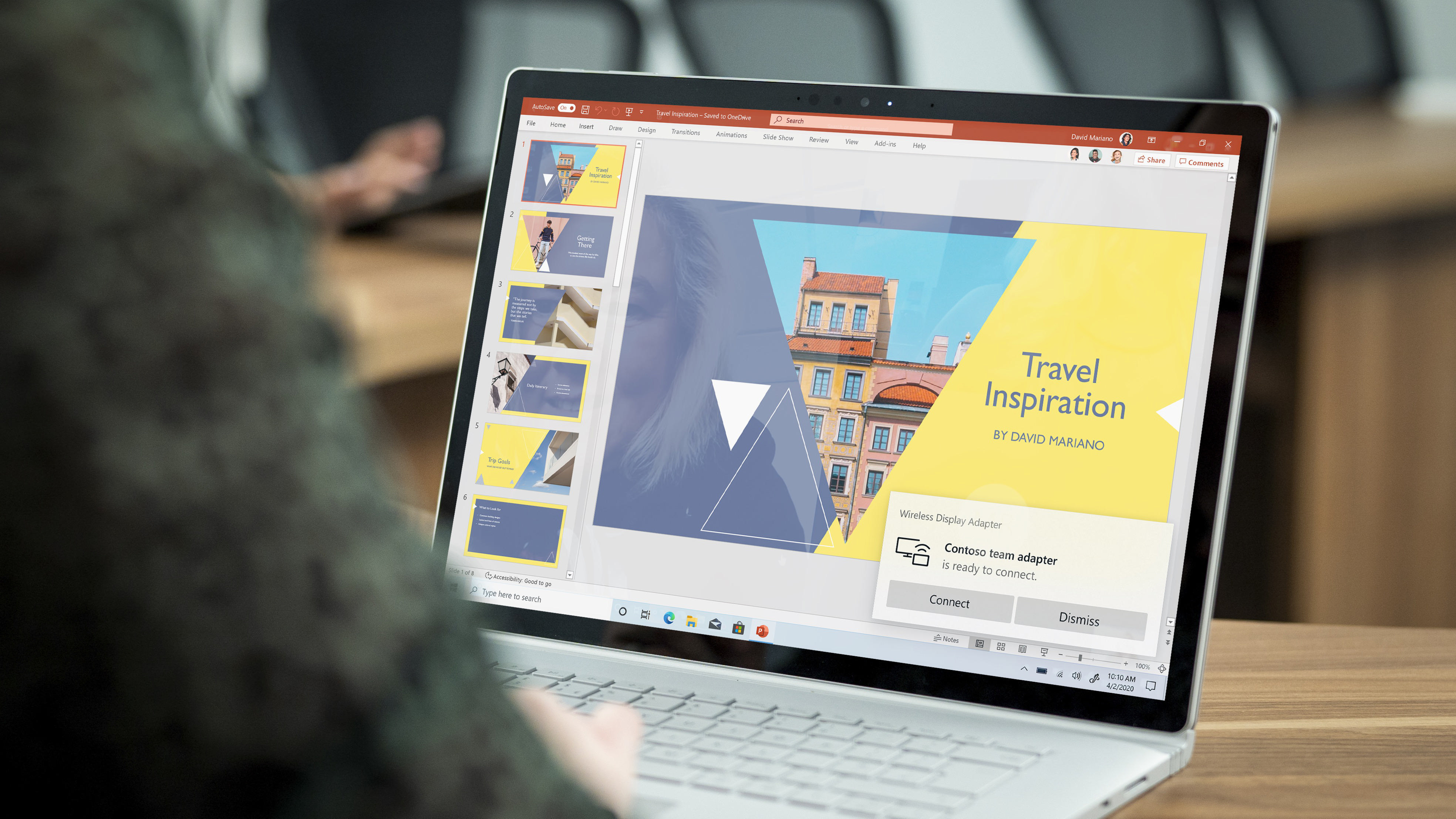 Person, die einen Laptop benutzt, auf dem eine Präsentation mit dem Text 'Travel Inspiration' und einer Gebäudefolie angezeigt wird.