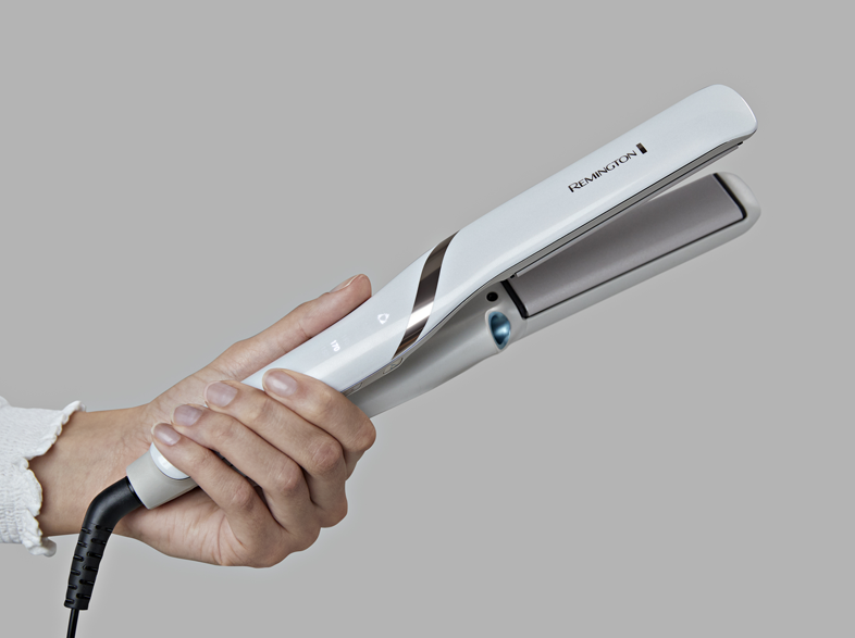 Egy személy egy fehér hajvasalót tart. A 'Remington' márkanév látható.
