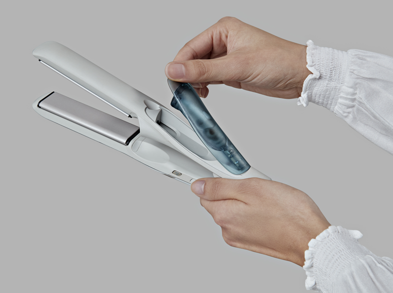 Kézben egy fehér hajsimító, kék vízkazettát helyeznek a készülékbe.