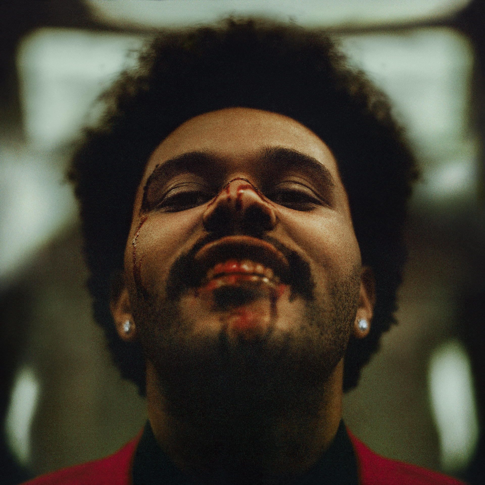 The Weeknd, közeli kép az arcáról. Véres orr, fekete göndör haj, piros öltöny.