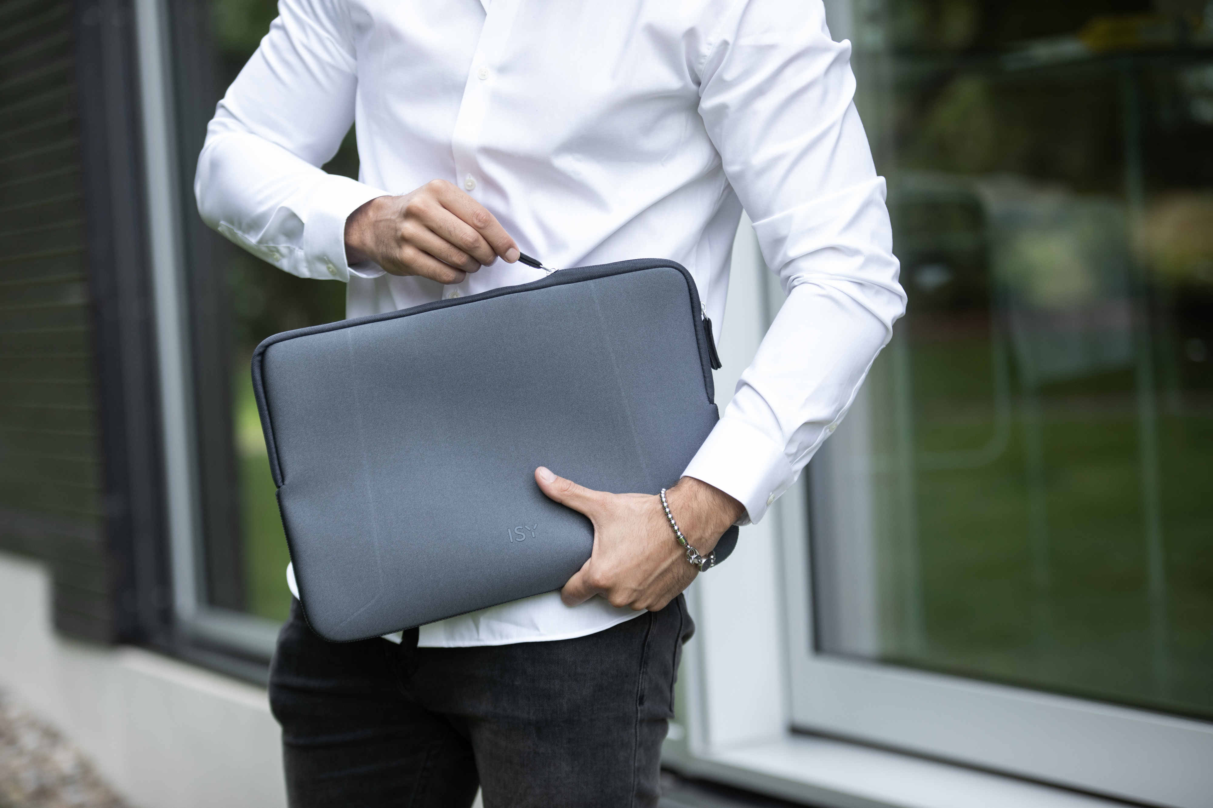 Ein Mann hält eine graue Laptop-Hülle. Er trägt ein weißes Hemd und eine schwarze Hose.