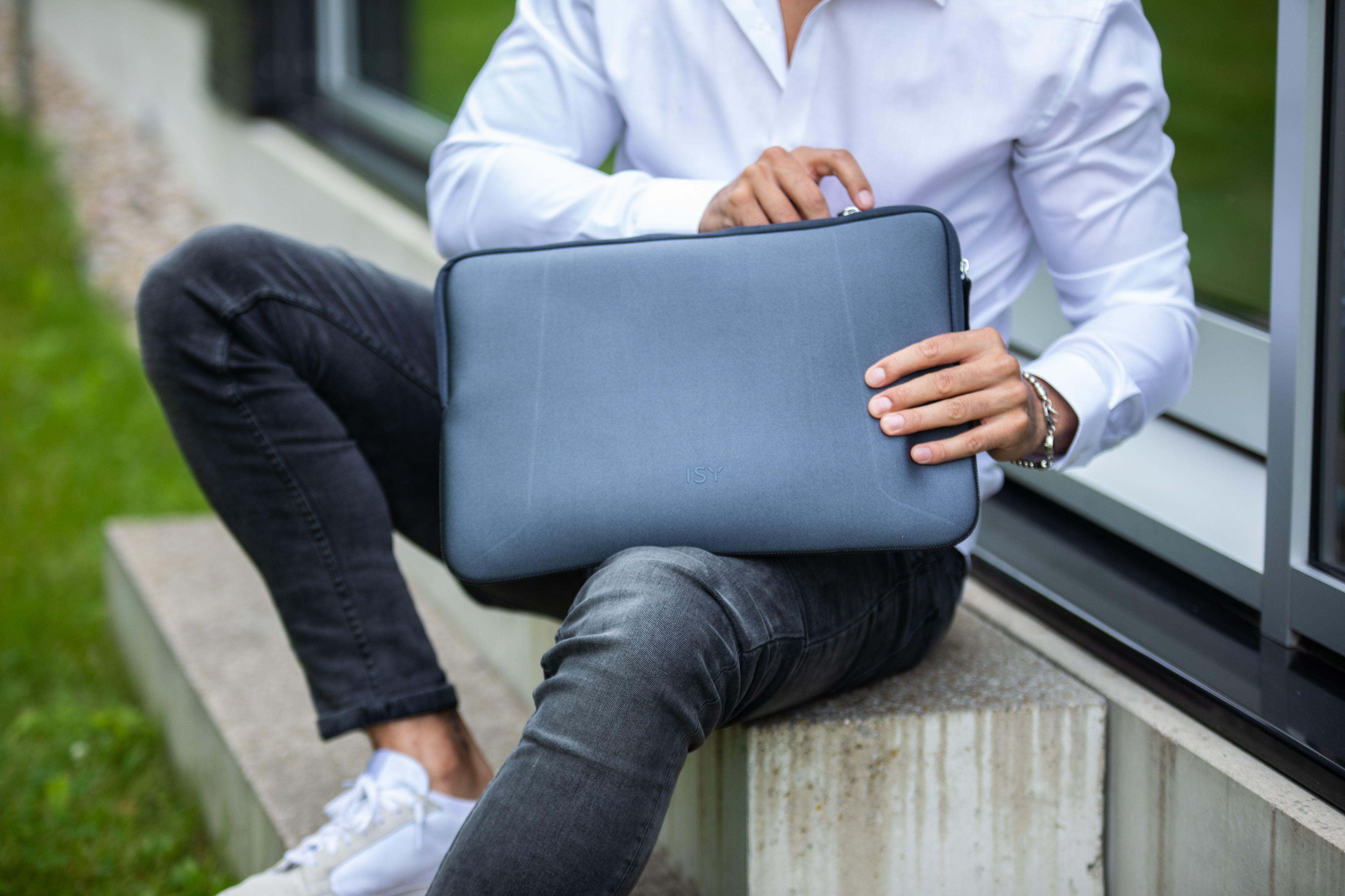 Mann hält eine graue Laptoptasche, während er draußen auf einer Betonstufe sitzt.