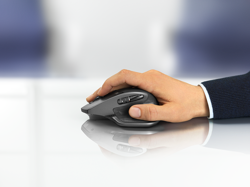 Main actionnant une souris sans fil gris foncé sur une surface blanche brillante.