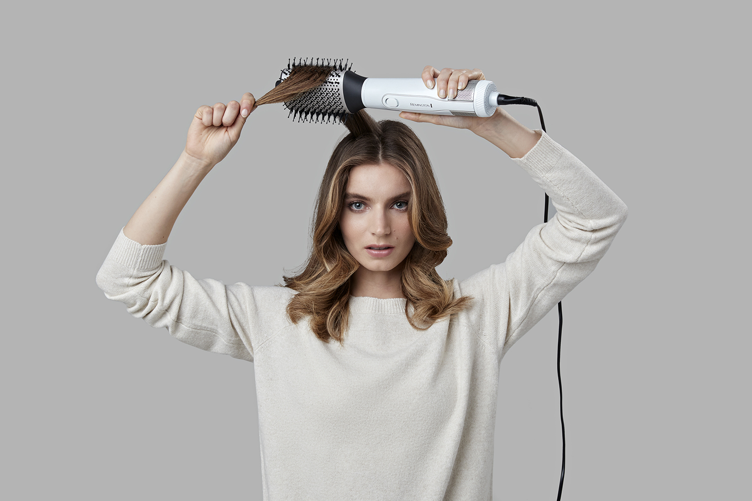 Een vrouw die haar haar stylet met een roterende haarborstel, kijkend naar de camera.