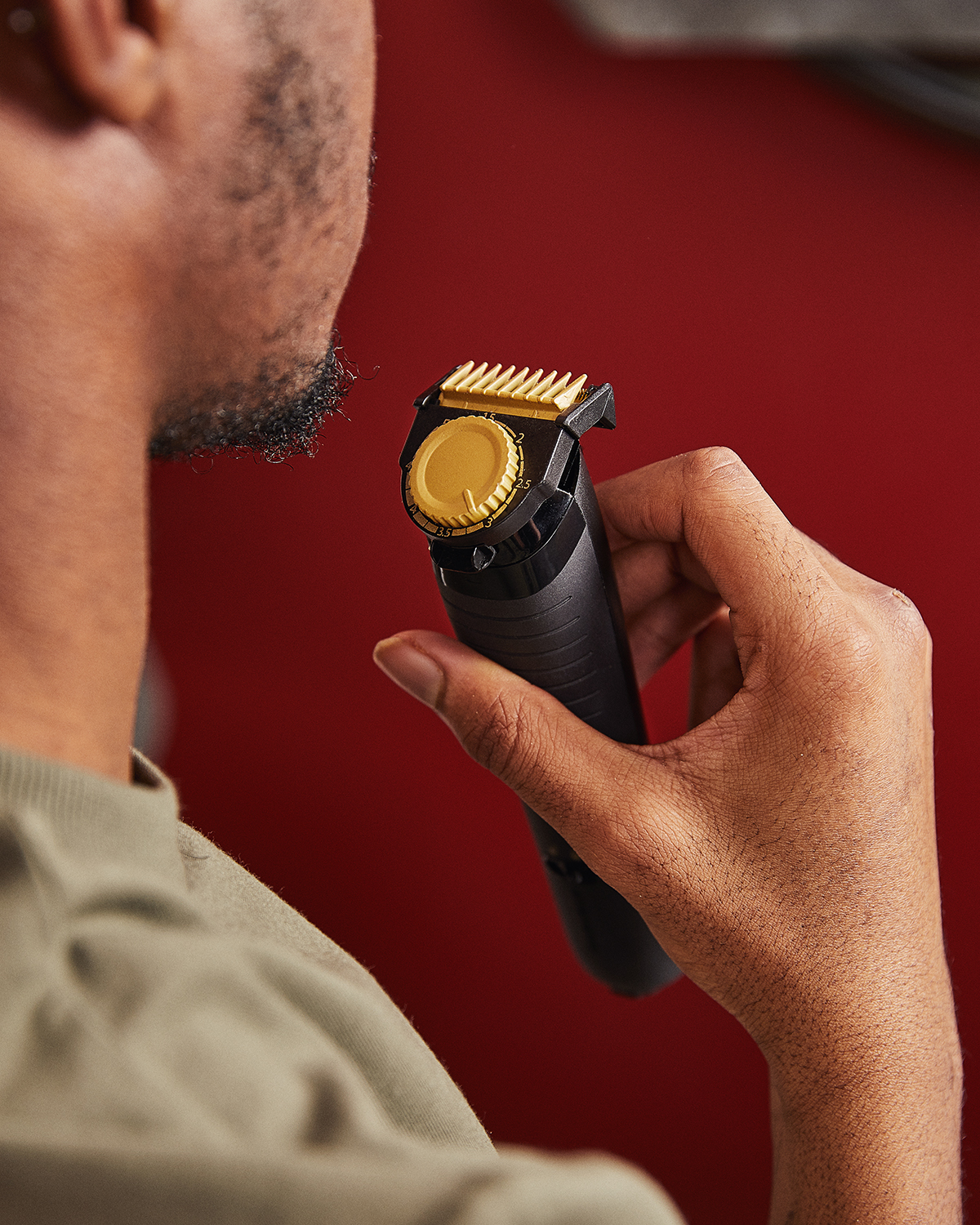 Man using a black and gold beard trimmer. The trimmer is held in his hand.