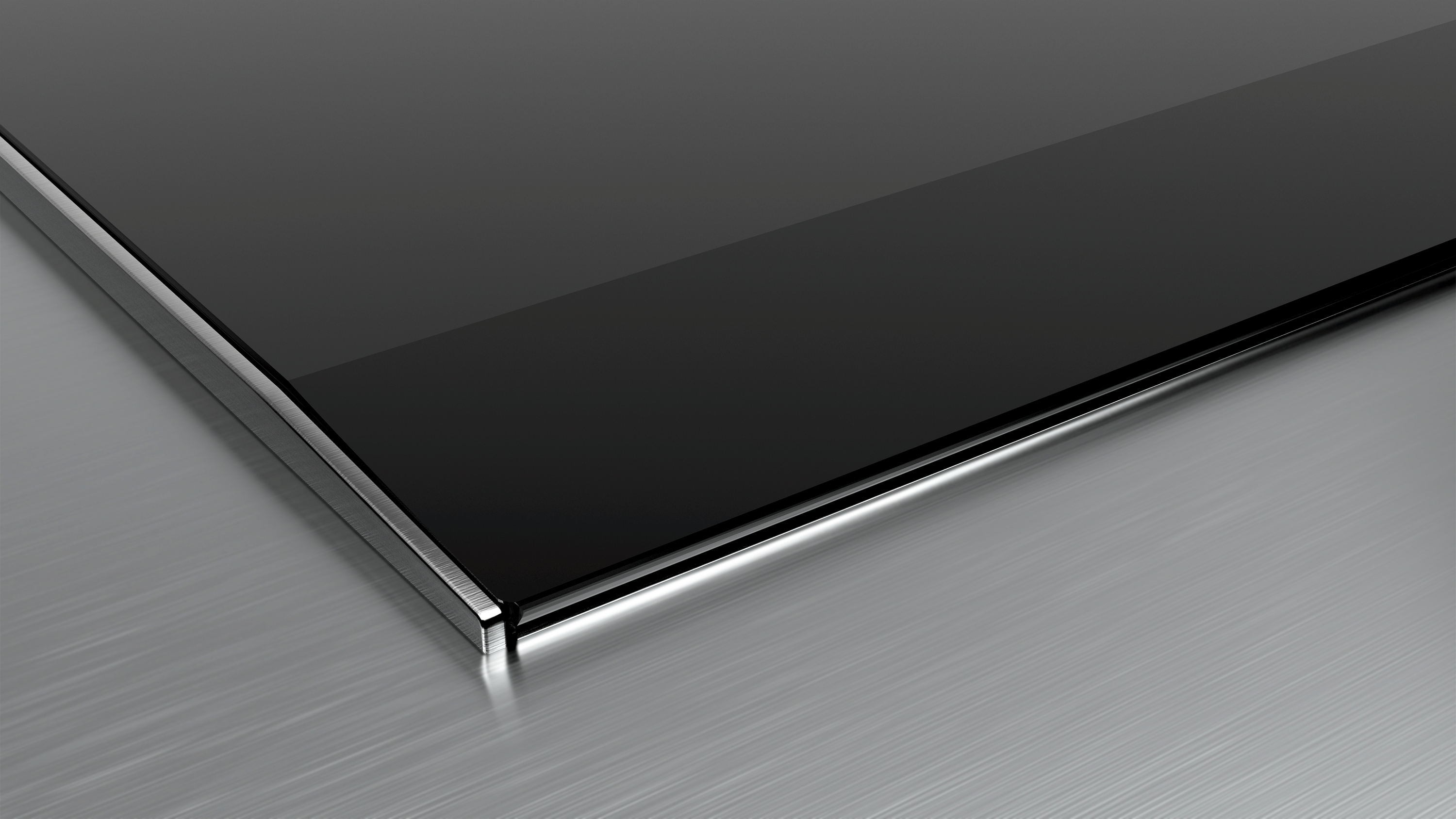 Gros plan sur une table de cuisson en verre noir avec un bord en acier inoxydable sur une surface argentée.