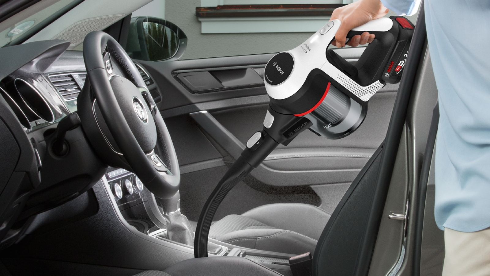 Hand saugt einen Autositz mit einem Bosch-Staubsauger ab.