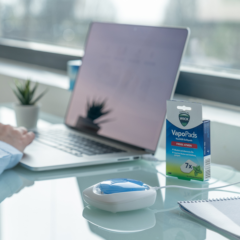 Eine Person arbeitet an einem Laptop, mit einer WICK VapoPads-Box und einem weißen Inhalator.