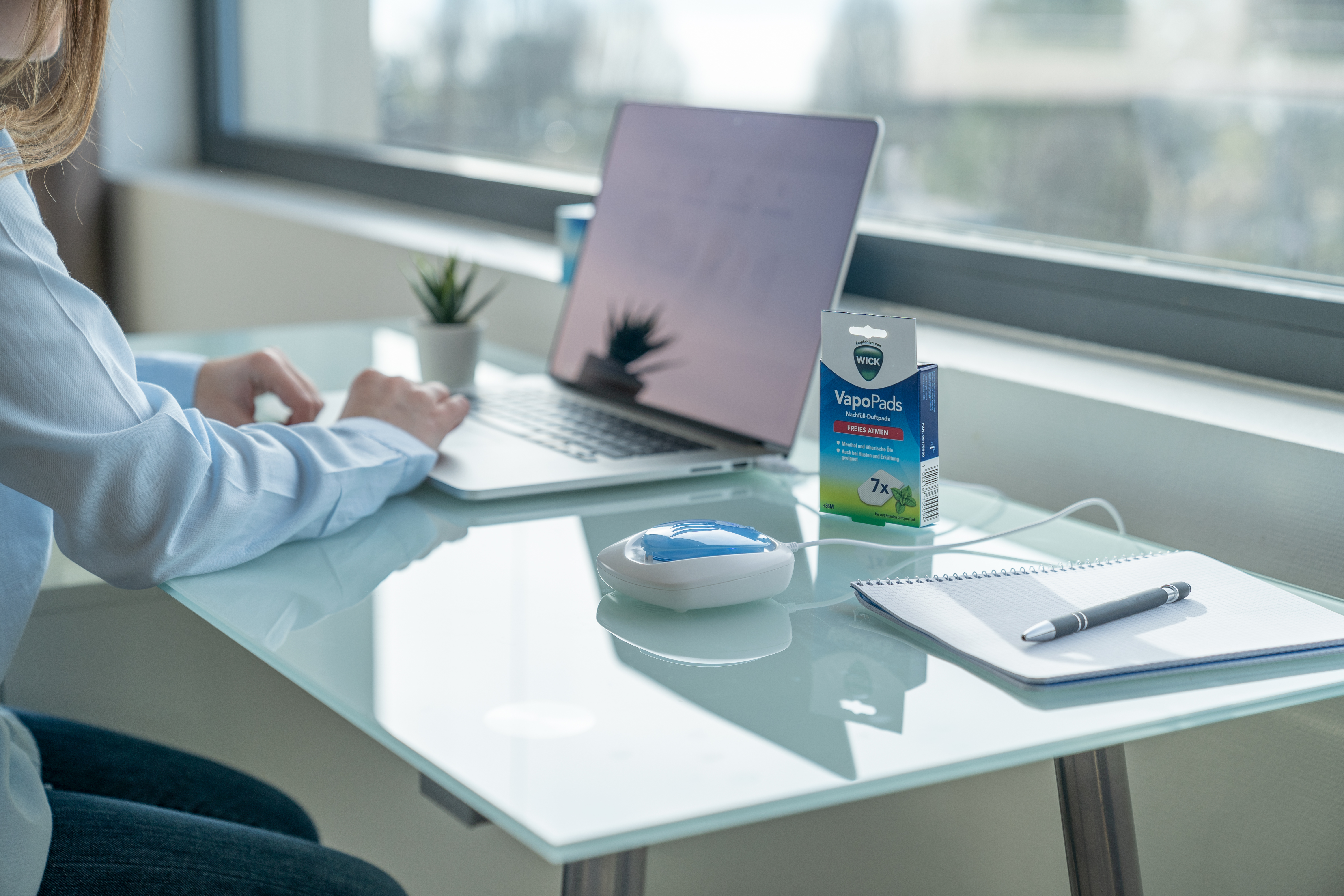 Eine Frau arbeitet an einem Schreibtisch mit Laptop, VapoPads und Notizblock.