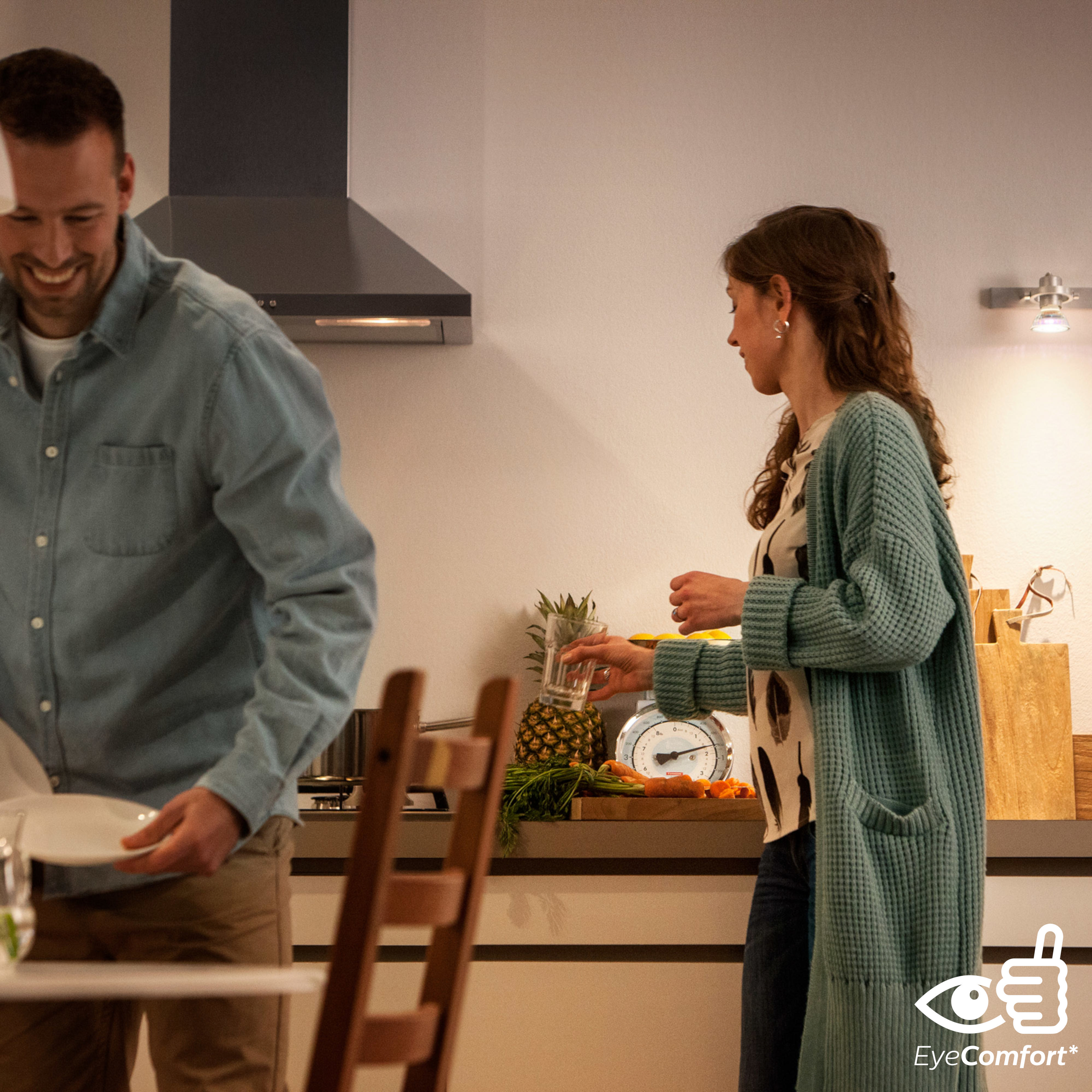 Ein Paar in einer Küche, das Essen zubereitet. Der Mann lächelt, die Frau hält ein Glas.