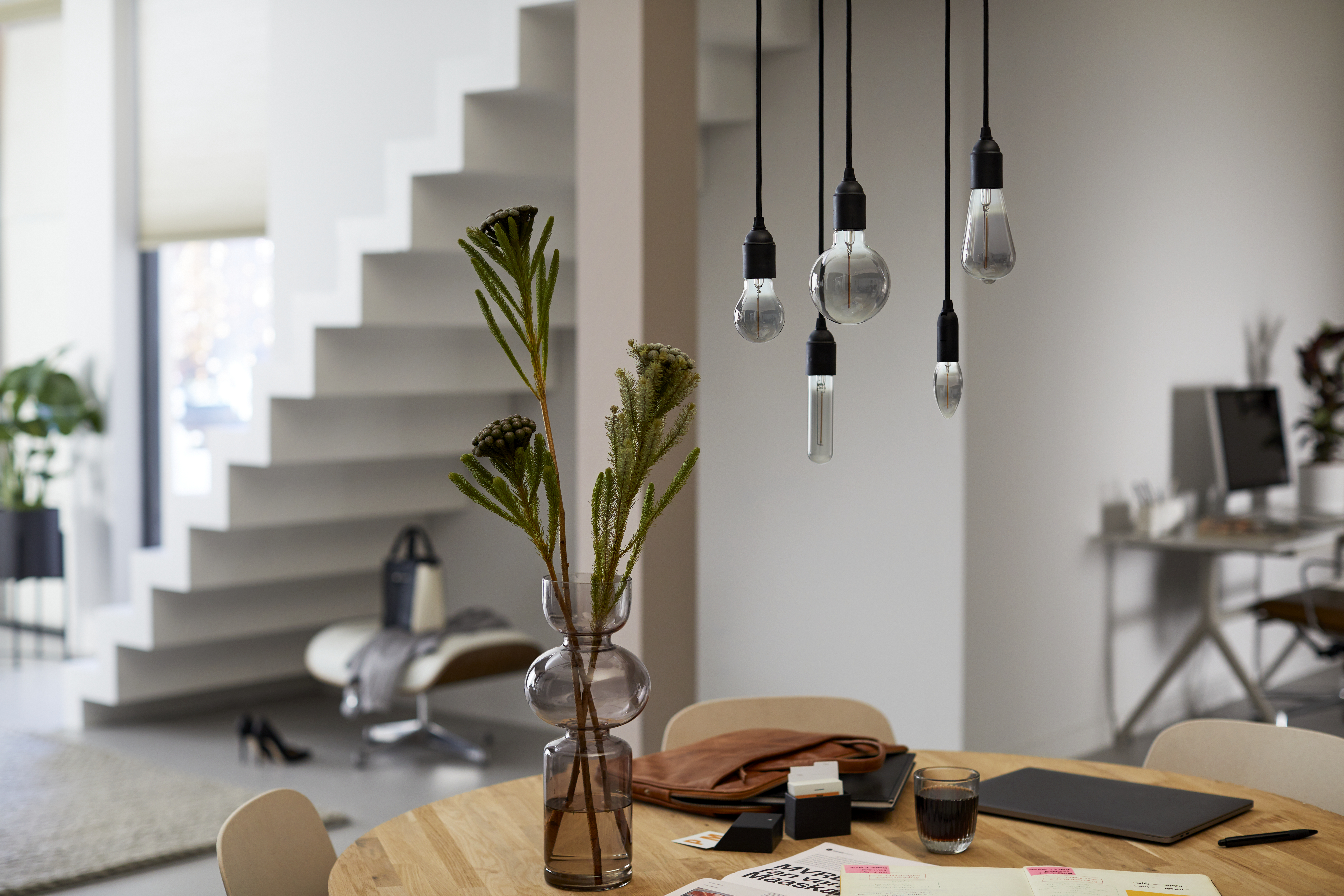 Modernes Esszimmer mit Hängelampen und einer Blumenvase. Treppe und Tisch sind in der Szene.