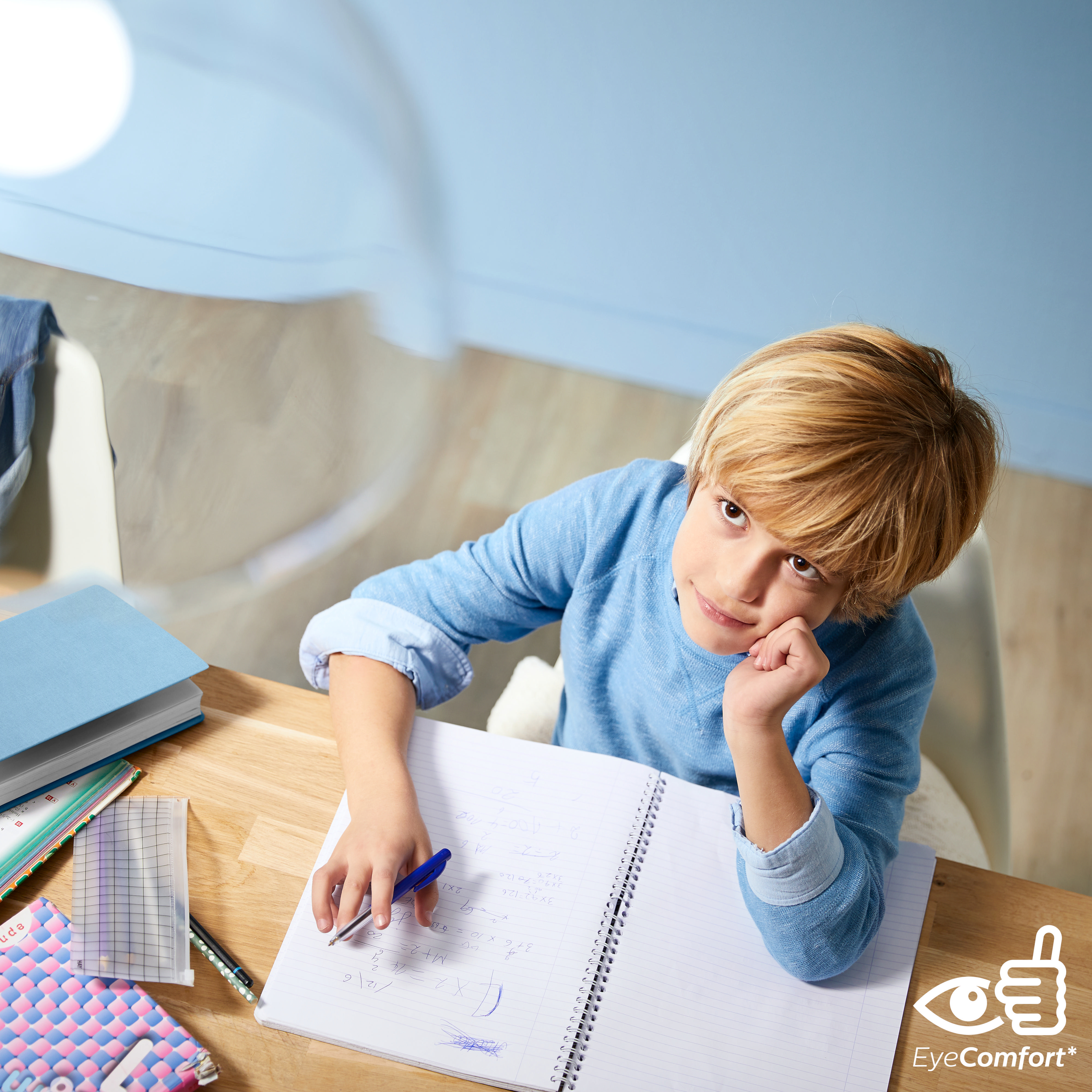 Junge lernt am Schreibtisch. Notizbuch, Bücher und Stift sind sichtbar. EyeComfort Label.