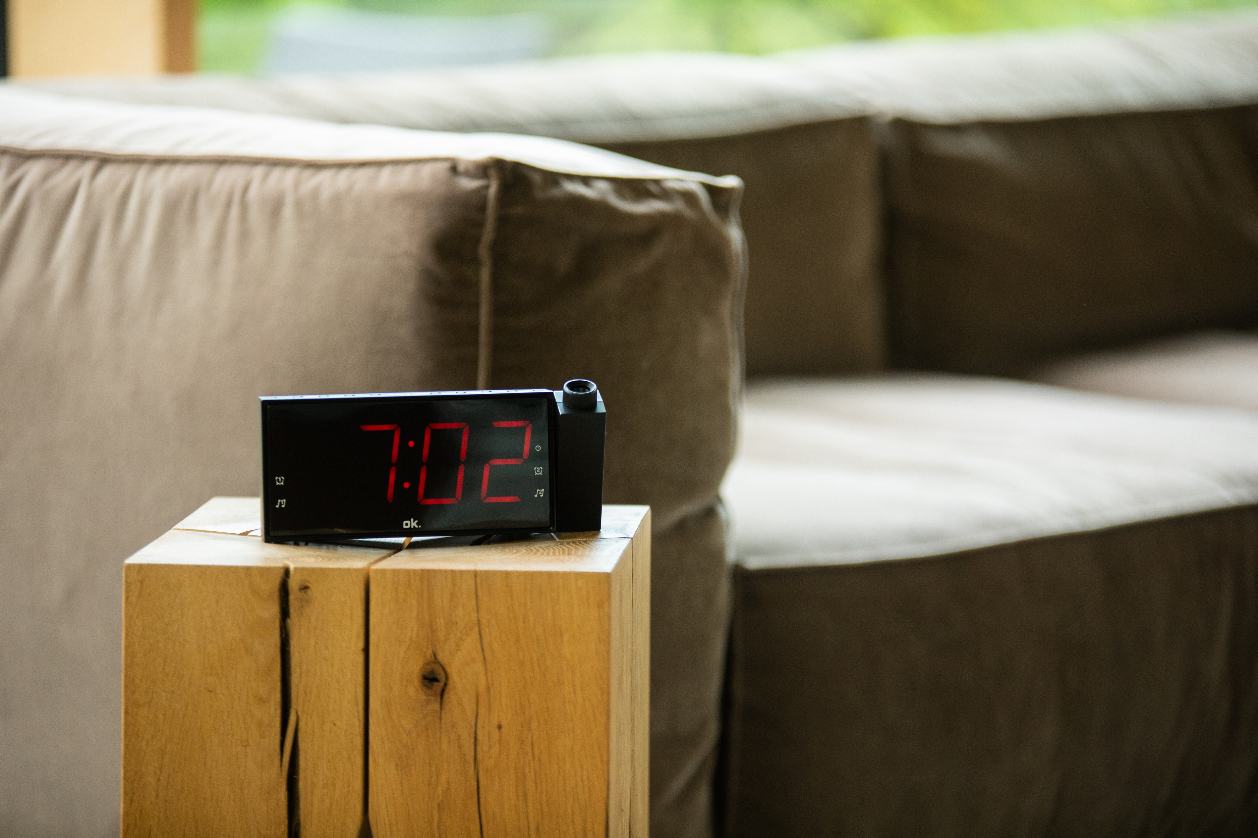 Schwarze Digitaluhr auf einem Holzständer, mit unscharfem Sofa im Hintergrund.