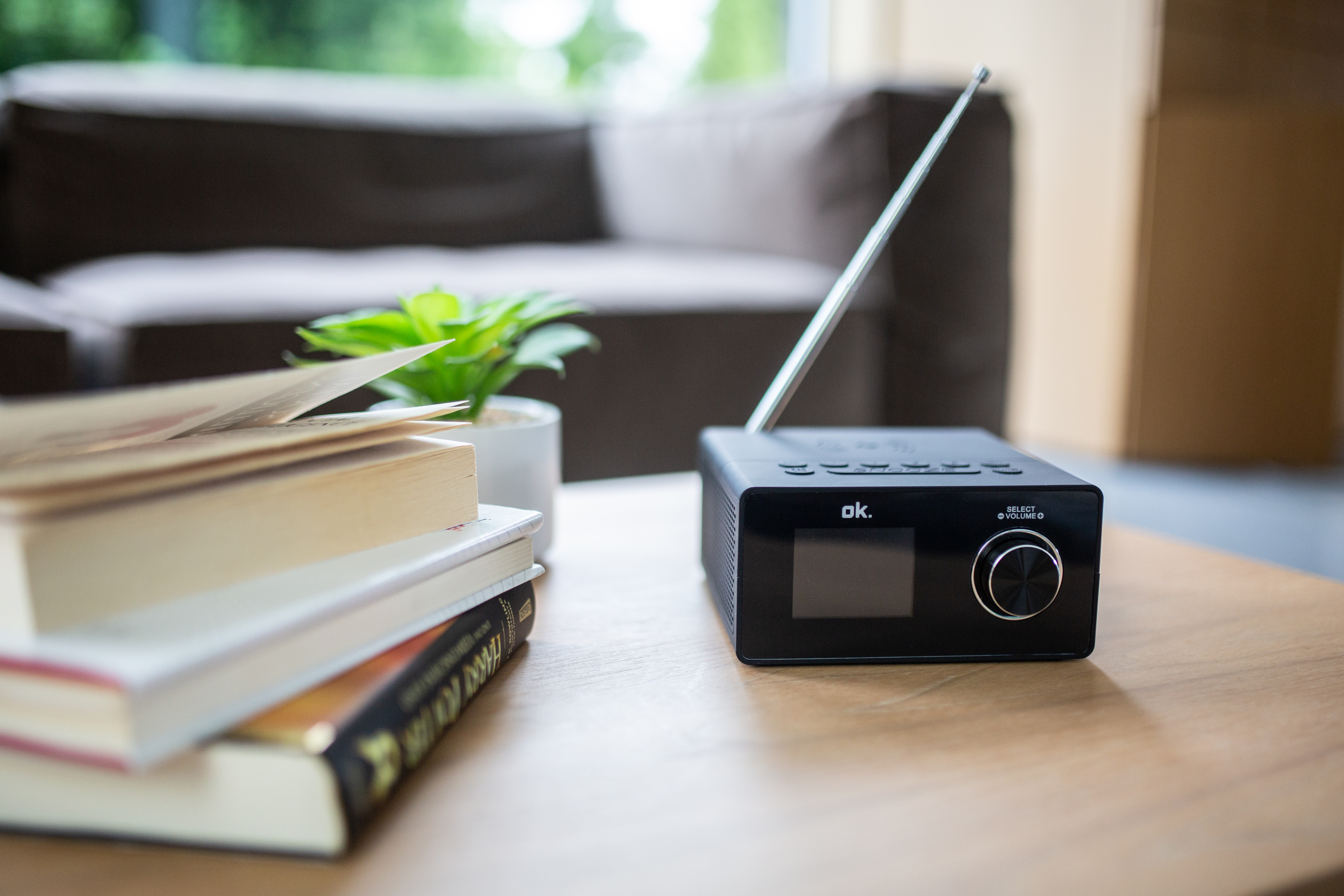Ein schwarzes Radio mit kleinem Bildschirm und ein Stapel Bücher auf einem Holztisch.