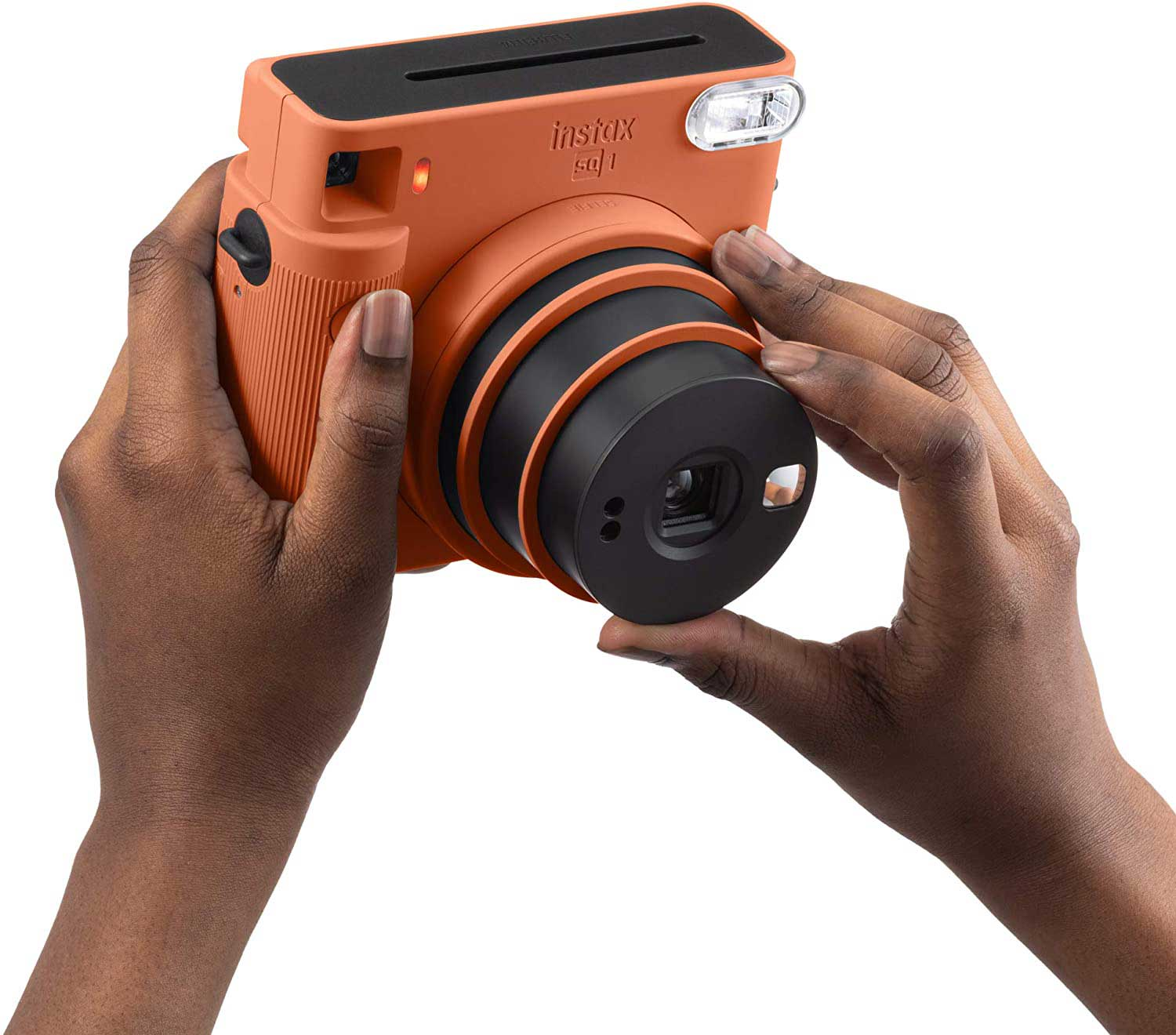 A person holds an orange Instax camera against a white background.