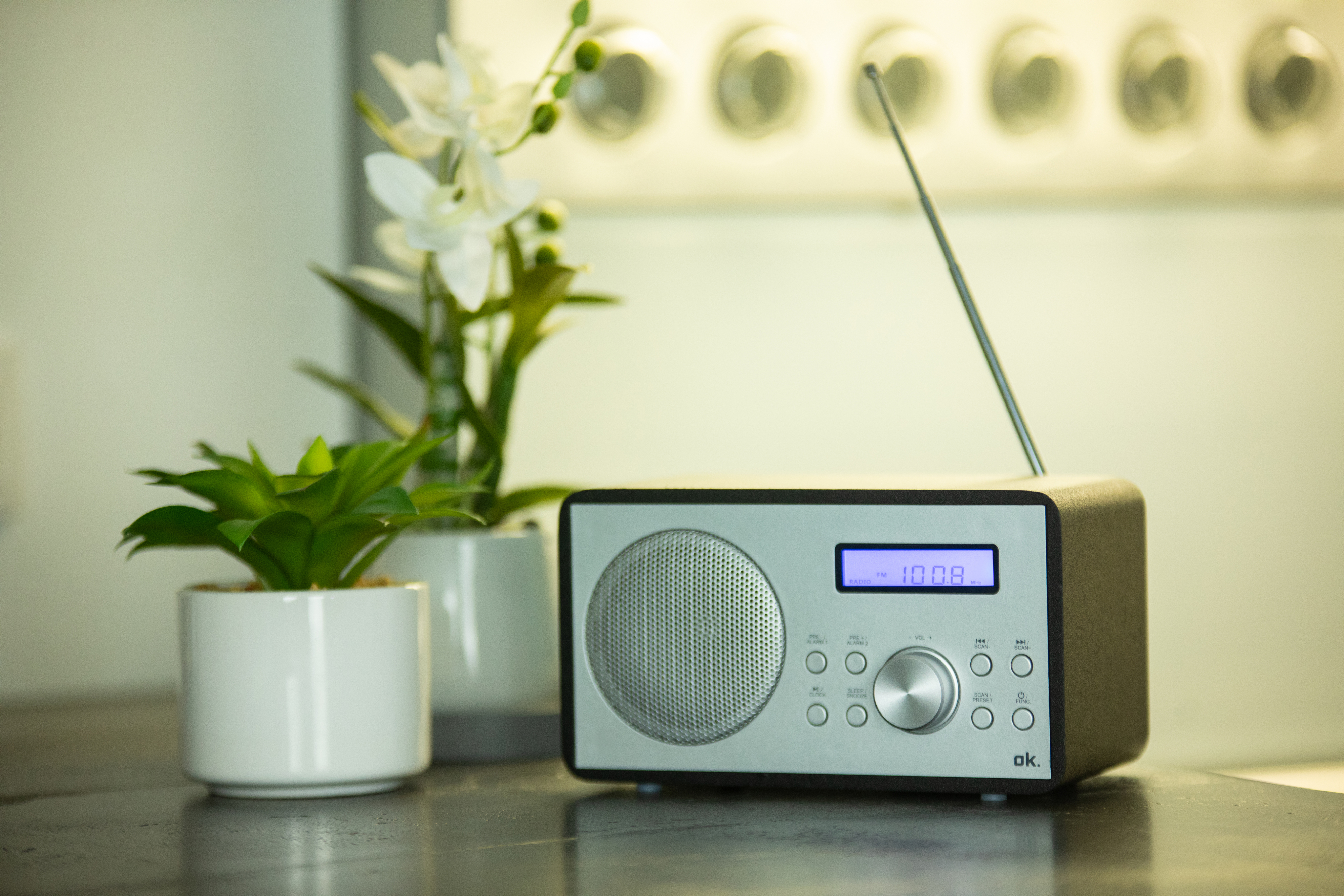 Ein silbernes und schwarzes Radio mit Display. Es hat eine kleine Antenne und steht auf einem Tisch.