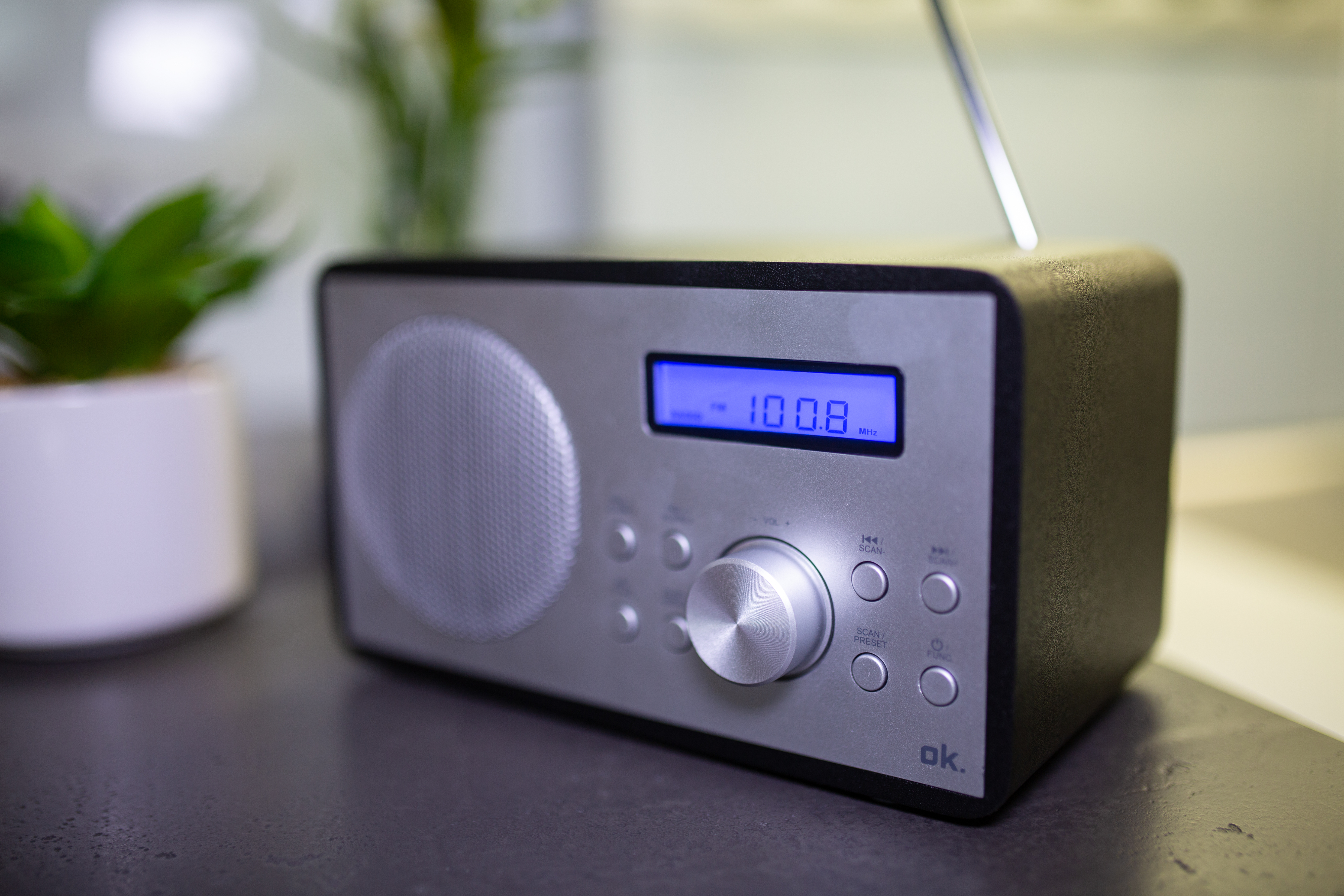 Ein silbernes Radio mit blauem Display und silbernem Knopf, auf Tisch.