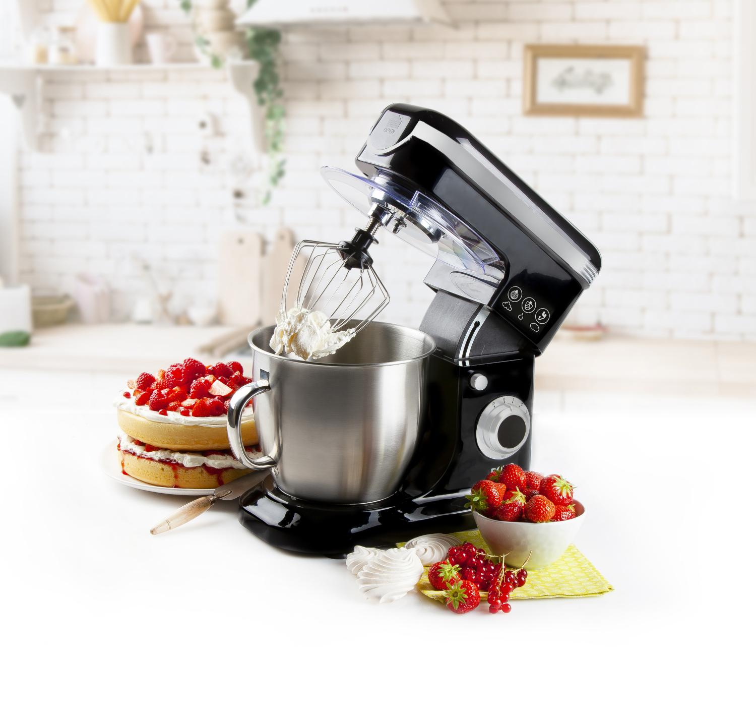 Black stand mixer with a bowl of whipped cream and strawberries. Cake on the side.