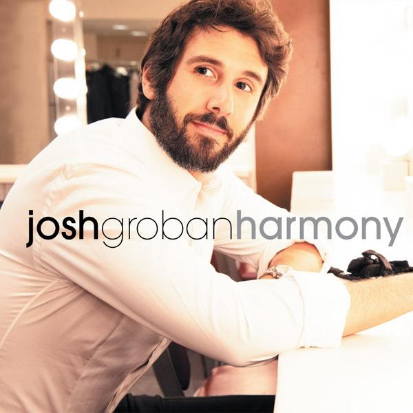 Josh Groban sitzt lächelnd an einem Tisch. Der Hintergrund umfasst Spiegel und Lichter.