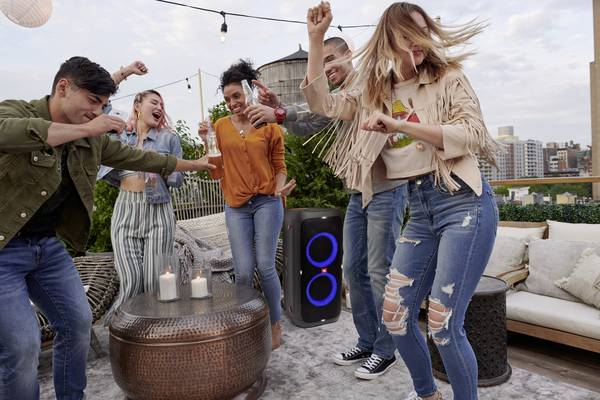 Un groupe de personnes danse sur un toit, une enceinte au milieu. Certaines personnes tiennent des boissons. Immeubles de la ville en arrière-plan.
