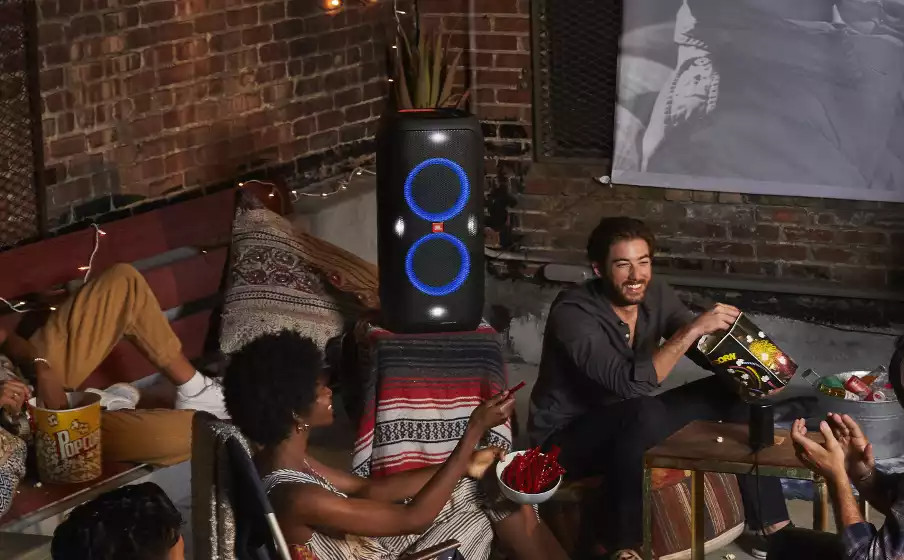 Un groupe de personnes profite d'une réunion avec un haut-parleur, du pop-corn et des boissons. Les gens sourient et rient.