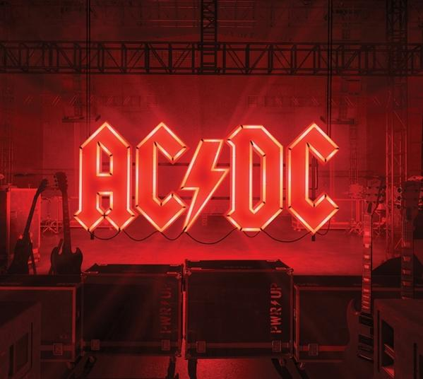 Logo AC/DC en néon rouge sur fond de scène. Scène noire avec équipement.